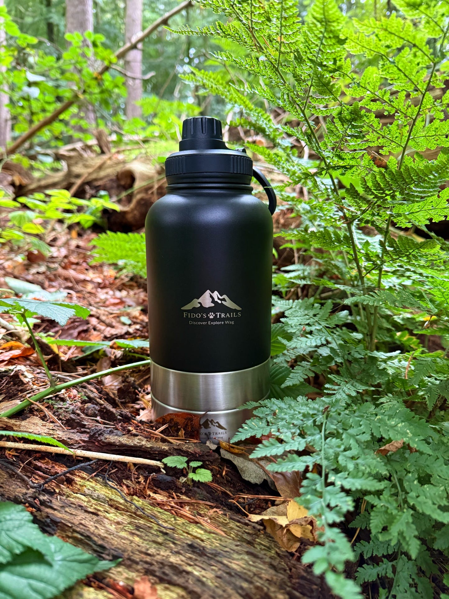 Black 3-in-1 dog water bottle placed on log in outdoor setting